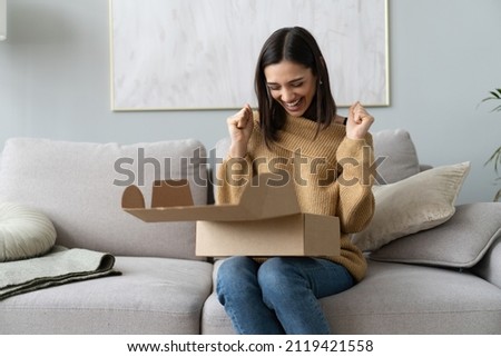 Happy young woman sit on couch in living room unpack cardboard box buying goods on Internet, smiling excited millennial girl open carton parcel order, shopping online, good delivery concept Royalty-Free Stock Photo #2119421558