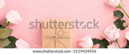 Valentine's Day design concept background with pink rose flower and wrapped kraft gift box on pink table background.