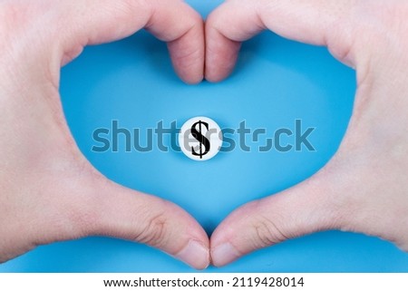 Medical pill with a dollar currency sign inside a heart made from hands on a blue background. The concept of a rise in price of medicines. Expensive treatment.