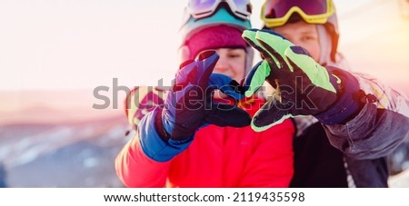 Snowboarders man and woman show heart sign with hands, winter travel love banner concept.