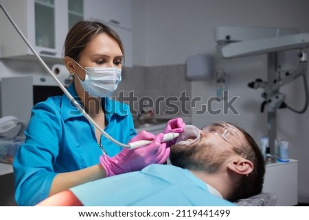 Macro photography. Top view on cleaning process in patient's mouth. Cleaning teeth with water jet and saliva ejector. Cheek retractor on the mouth. Concept of professional dental hygiene.