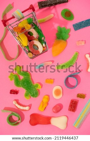 marmalade sweets, a background of various kinds of jelly sweets in the form of bears, ribbons, fruits and other toys. Candies in a toy shopping cart. On a pink background.