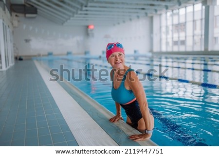 Happy senior woman in swimming pool, leaning on edge.
