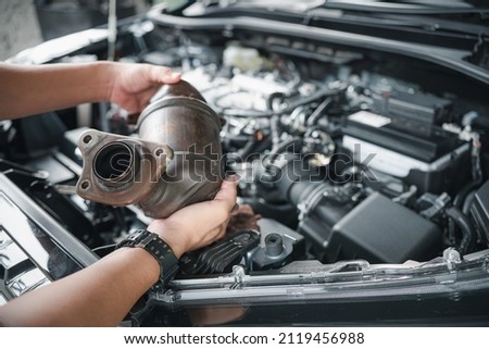 Close up old catalytic converter in hand Car service man remove from engine gasoline car dust clogged condition on filter in service concept and engine room in the background Royalty-Free Stock Photo #2119456988