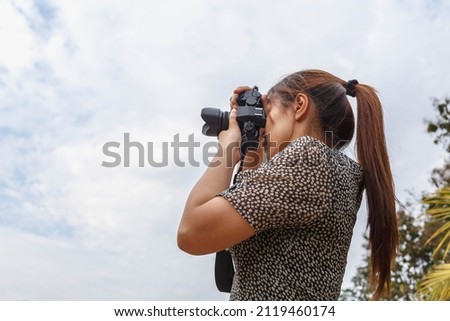 A young woman photographer holding a camera is taking pictures intently.