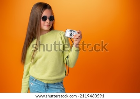 Beautiful teen girl with old photo camera against orange background