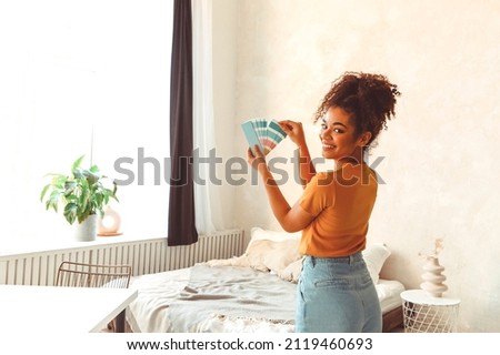 Smiling African American girl stands back to camera in middle of bed room with palette of blue shades for interior renovation, choosing paint for balance of mind and body, refreshing indoor design Royalty-Free Stock Photo #2119460693