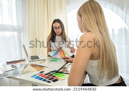 two beautiful girls designers sit at a table and choose colors for the design of rooms. Design concept. The concept of colors