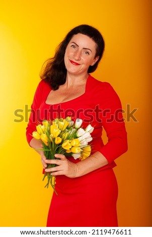 a 50-year-old woman with a bouquet of yellow tullans in a red dress on a yellow background in isolation with a space for text on Valentine's Day on March 8