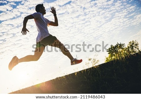 Silhouette of young man running sprinting on road. Fit runner fitness runner during outdoor workout with sunset background.	