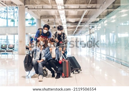 Young happy friend traveler in quarantine for coronavirus wearing surgical mask face protection look at camera making live selfie on smartphone before long travel vacation flight at airport