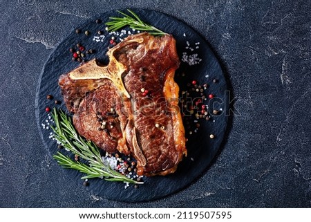 fried porterhouse steak, t-bone steak with thyme, rosemary and peppercorn on black plate on concrete table horizontal view from above, flat lay, free space Royalty-Free Stock Photo #2119507595