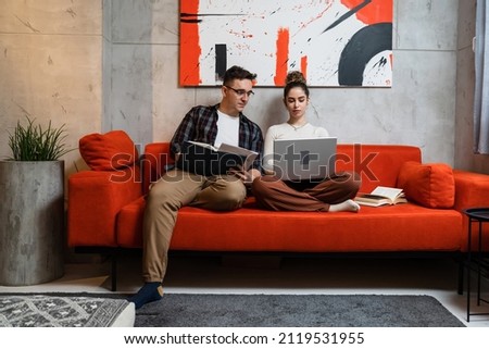 Man and woman young adult couple generation Z sitting together on the sofa bed at home study male and female friends helping each other with lesson tutor and student learning education concept