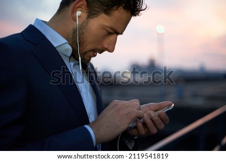 Businessman wearing a suit and earbuds in the city centre during dawn sunrise