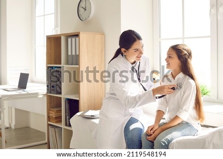 Smiling doctor checking child's lungs during medical checkup in modern sunny exam room at the clinic. Friendly female pediatrician using stethoscope to examine breathing and heartbeat of young patient Royalty-Free Stock Photo #2119548194