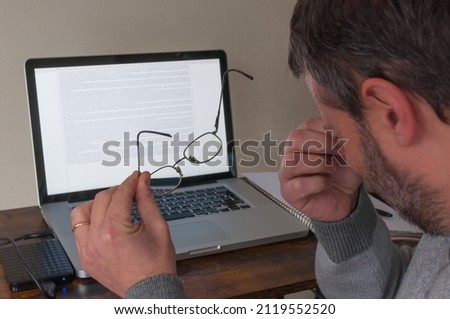 man works on a laptop and takes off his glasses because his eyes are bothering him. Glasses in foreground, laptop in background Royalty-Free Stock Photo #2119552520