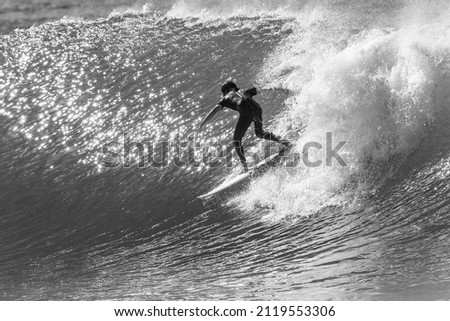 Surfing surfer rides sunlight reflecting ocean wave unrecognizable male rear behind action black and white photo  . Royalty-Free Stock Photo #2119553306