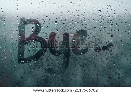 Word BYE written on wet glass on a rainy day