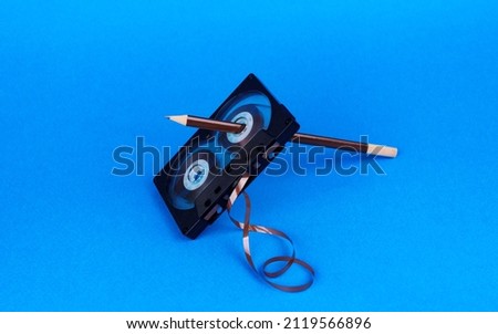Old audio cassette with a pencil in the hole on a blue background