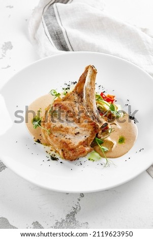 Roasted pork steak with vegetables garnish and sauce. Bone-in ribeye pork chops. Main course of pork in rustic style Royalty-Free Stock Photo #2119623950