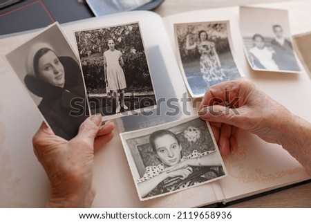 Old hands. Senior woman is looking her own photos were taken in 1955 ,1957,1967. Retired person has got smile while remembering how young she was. Selective focus. 