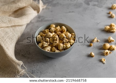 Golden airy popcorn in a gray plate on a concrete table on a piece of light burlap, fried crispy corn for watching a movie or series