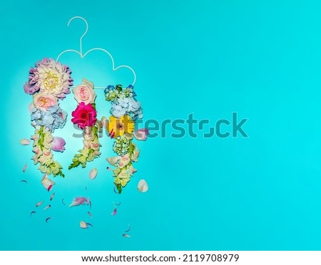 fresh flowers arranged as rain drops falling from a clothes hanger isolated over bright blue background, weather, summer of creative concept. High quality photo