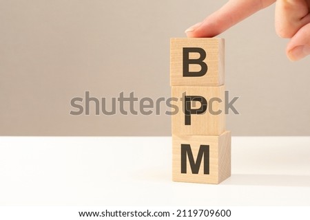 the hand puts a wooden cube with the letter BPM, business concept. BPM - short for Business Process Management Royalty-Free Stock Photo #2119709600