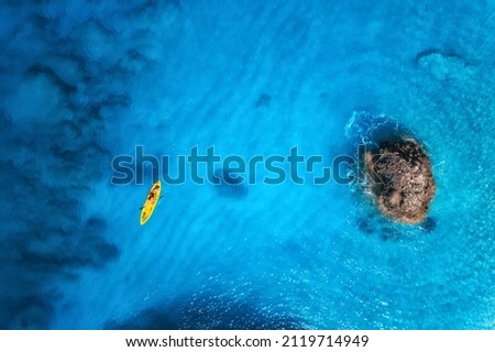 Aerial view of yellow kayak in blue sea at sunset in summer. Man on floating canoe in clear azure water, rocks, stones. Lefkada island, Greece. Tropical landscape. Sup board. Active travel. Top view Royalty-Free Stock Photo #2119714949