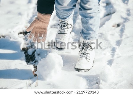 The girl actively rolls a snowball and sculpts a snowman in the winter season