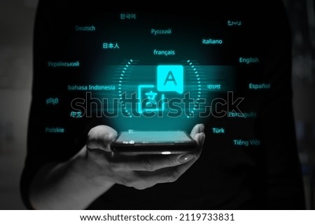 The name of the language with translation to the original. The person is holding a smartphone with a hologram. Royalty-Free Stock Photo #2119733831