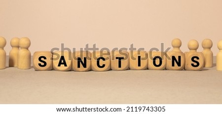 Wooden cubes with the word SANCTION stand on a wooden background between a magnifying glass and a pen.