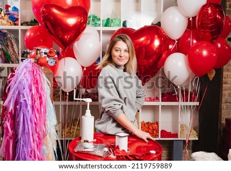 a woman aerodesigner with a composition of white, red, foil balloons in the form of a heart and ball in the store. sale of balloons for festive decoration.