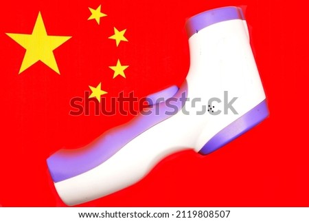 Concept of winter Games in 2022 in Beijing, China, due to threat of new coronavirus infection. Infrared digital thermometer on background red s Chinese flag. Copy space