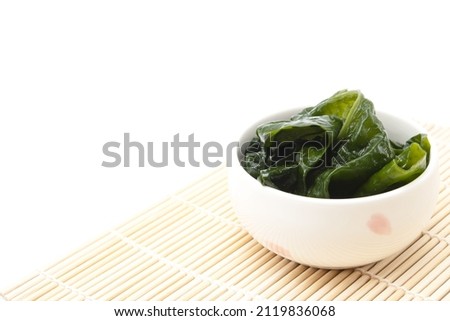 Seaweed wakame in ceramic bowl on bamboo mat isolated on white background. Japanese food