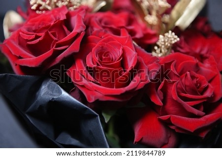 Bouquet of red roses with golden decorative branches in a black package