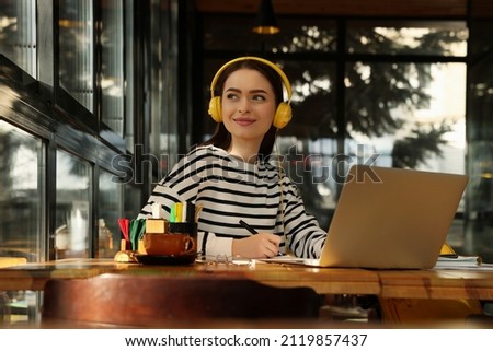 Young female student with laptop and headphones studying at table in cafe Royalty-Free Stock Photo #2119857437