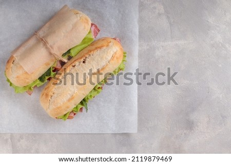 Top view of two banh mi sandwich with sliced grilled pork and peppers and salad packed in paper on white paper. With copy space. Royalty-Free Stock Photo #2119879469
