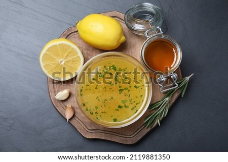 Bowl with lemon sauce and ingredients on dark table, top view. Delicious salad dressing Royalty-Free Stock Photo #2119881350