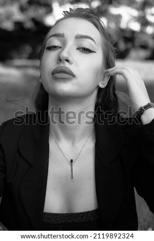 Black and white portrait of a young girl in the city park. Elegant and melancholy portrait, the girl is sitting on the grass. Beautiful woman in classic clothes