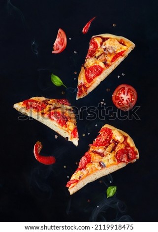 Pieces of pizza flying with herbs, sauce and spices on a dark background with smoke