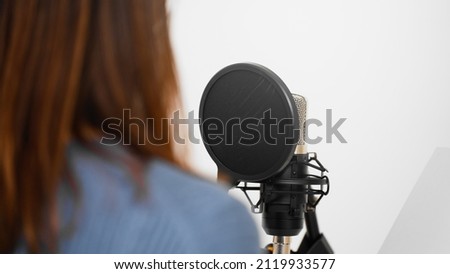 A young woman recording in front of a microphone.