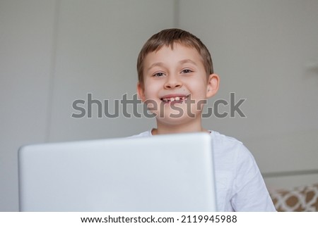 Cute schoolboy doing homework on the bed. A little boy of 7 years old is doing tasks online. Home schooling. Cozy.