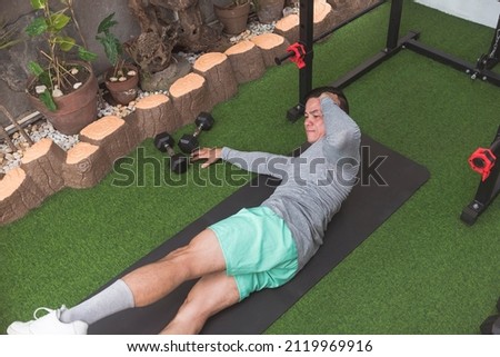 A fit asian guy does oblique crunches while lying on a black mat. Leg raised for added challenge. Working out his midsection and core at his home gym. Royalty-Free Stock Photo #2119969916