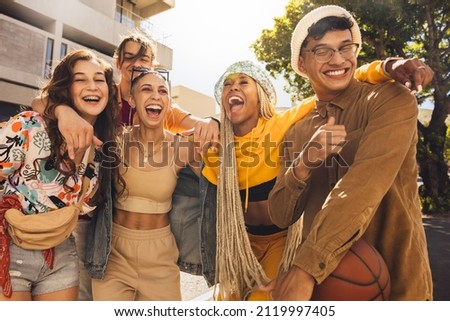 Group of generation z friends laughing together outdoors. Cheerful young friends embracing each other in the summer sun. Youngsters having fun and enjoying their youth. Royalty-Free Stock Photo #2119997405
