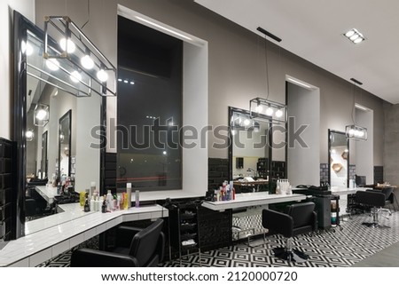 Modern interior of the barbershop with mirrors, chairs and other equipment near large windows in the evening. Royalty-Free Stock Photo #2120000720