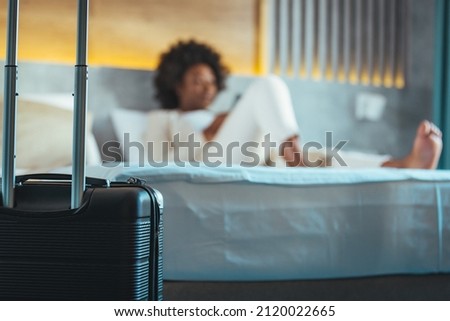 A young business woman lying in a hotel room using a mobile phone. A woman lies in a hotel room and reserves a taxi using a smartphone. Conceptual of travel and vacation.