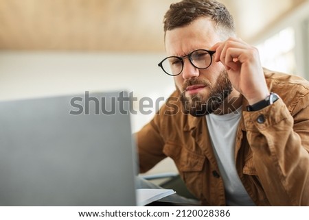 Poor Eyesight. Man Looking At Laptop Computer Squinting Eyes And Wearing Eyeglasses Having Problem With Sight, Frowning Reading Negative News Sitting At Home. Selective Focus Royalty-Free Stock Photo #2120028386