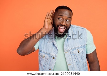 Photo of excited afro guy wear denim vest hearing secrets empty space isolated orange color background Royalty-Free Stock Photo #2120031440