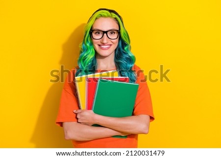 Photo of pretty shiny young vibrant woman wear orange t-shirt spectacles smiling embracing book stack isolated yellow color background